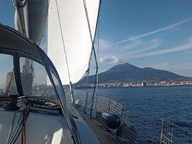 A stunning view of a sailboat underway with the majestic Mount Vesuvius in the background, showcasing the beauty of sailing along the coastline.