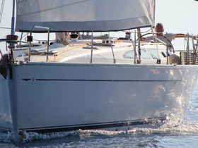 A sleek sailboat glides through the water with a crew member at the helm, showcasing the beauty of sailing on open waters.