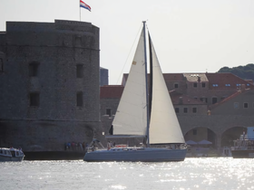 A beautiful sailboat glides through the shimmering waters of a harbor, with historic stone architecture in the background, showcasing the charm of coastal destinations.