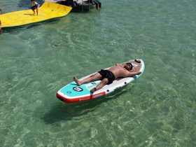 A relaxing day on the water with a man sunbathing on a paddleboard while a child enjoys the fun on a floating mat — perfect for summer adventures and family outings.