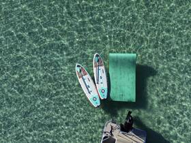 A serene aerial view showcasing paddleboards and a floating mat resting on crystal-clear waters, perfect for a day of relaxation and fun on the water.