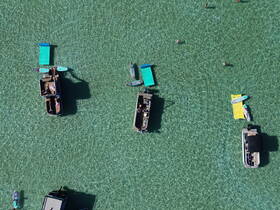 A vibrant scene at a sandbar with multiple boats and people enjoying swimming and paddleboarding in crystal-clear waters — a perfect day for water activities.