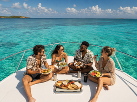 A group of friends enjoys a delicious meal on the deck of a yacht, surrounded by stunning turquoise waters — perfect for a memorable day on the water.