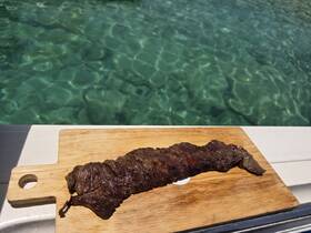A delicious grilled steak displayed on a wooden cutting board, perfect for enjoying a meal on the water. The clear turquoise water in the background enhances the boating experience.