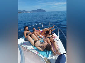 A group of friends relaxes and sunbathes on the bow of a boat, enjoying a perfect day on the water with stunning views in the background.