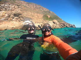 Two snorkelers enjoy a vibrant underwater adventure, capturing the excitement of exploring marine life against a stunning rocky backdrop.
