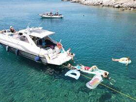 A lively group enjoys a sunny day on the water, relaxing on floating mats and swimming around a yacht — the perfect setting for summer fun and aquatic adventures.