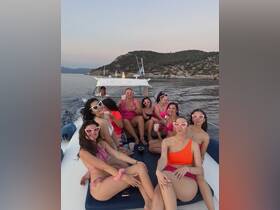 A lively group of friends enjoys a fun day on the boat, celebrating with drinks and laughter against a beautiful coastal backdrop.