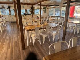 Interior view of a spacious dining area on a boat, featuring wooden tables and white chairs, perfect for group gatherings and dining experiences on the water.