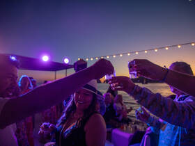 A lively group toasts with cocktails against a stunning sunset backdrop, capturing the essence of celebration and fun on the water.