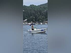 A young man navigates a small speedboat through calm waters, showcasing the joy of boating in a scenic coastal area.