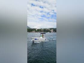 A young man navigates a small boat through calm waters, showcasing the scenic backdrop of a coastal town — perfect for exploring the beautiful shoreline.