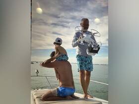 A family enjoys a fun moment on a boat, with a child on an adult's shoulders while another adult prepares to fly a drone — capturing memories on the water.