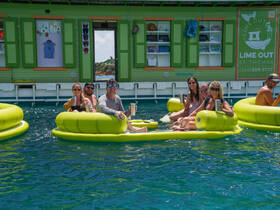 A lively group enjoys drinks on floating mats in the vibrant waters of St. Thomas, capturing the essence of a fun day at Lime Out.