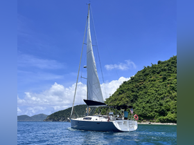 A beautiful sailboat glides through clear waters, showcasing its elegant design against a backdrop of lush green hills — perfect for sailing adventures.