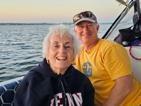 A joyful couple smiles for the camera while enjoying a scenic boat ride at sunset, capturing a perfect moment of relaxation and happiness on the water.
