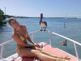A woman enjoys a sunny day on a boat with pelicans nearby, showcasing a delightful interaction with wildlife in a picturesque setting.