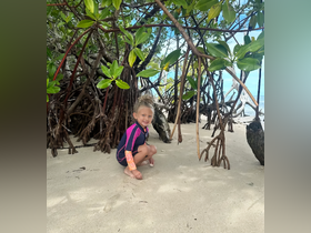A joyful child plays in the sandy area beneath mangrove trees, capturing the essence of fun and exploration in a tropical beach setting.