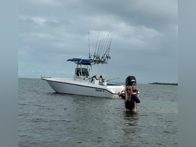 A joyful moment captured as a mother carries her child in shallow water near a fishing boat, showcasing a fun family day on the water.