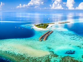A stunning aerial view of a tropical island surrounded by crystal-clear turquoise waters, showcasing the beauty of the coastline and nearby boats — perfect for vacation inspiration.
