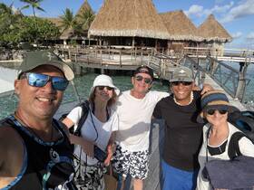 A cheerful group of friends poses for a selfie on a tropical dock, capturing the essence of their vacation experience in paradise.