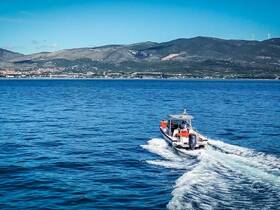 A sleek speedboat navigates through clear blue waters, showcasing its design and the stunning coastal landscape in the background.