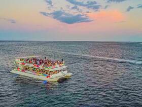 A vibrant party boat filled with guests enjoying a sunset cruise, creating a lively atmosphere on the water.