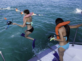 Two women prepare to jump into the water for snorkeling, showcasing the excitement of on-water activities and group fun during a boating adventure.