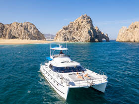 A couple relaxes on the deck of a luxurious yacht, surrounded by stunning rock formations and a beautiful beach — an ideal setting for a day of sun and relaxation on the water.