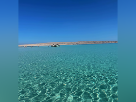 A stunning view of turquoise waters with a boat anchored nearby and people enjoying the beach, perfect for a relaxing day in paradise.
