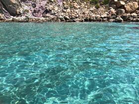 A serene view of clear turquoise waters with rocky shores in the background, ideal for showcasing beautiful coastal destinations.