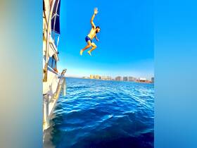 A man leaps off the side of a boat into the sparkling ocean, capturing the thrill of summer adventures on the water.