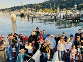 A joyful group of friends and family gathers on the dock, celebrating together with smiles and laughter, surrounded by a picturesque marina backdrop.