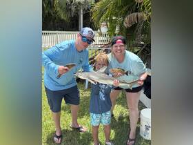 A family proudly displays their fishing catch, including a shark, showcasing a fun day of fishing together. Perfect for family adventures and wildlife encounters.