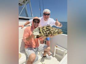 Two anglers proudly display their impressive catch aboard a fishing boat, showcasing the excitement of a successful day on the water.