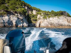 A scenic view of a boat cutting through clear waters along a rocky coastline, showcasing the beauty of nature while underway.