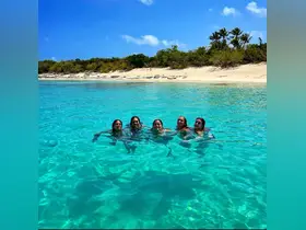 A joyful group of friends swims in the crystal-clear turquoise waters, enjoying a perfect beach day under the sun.