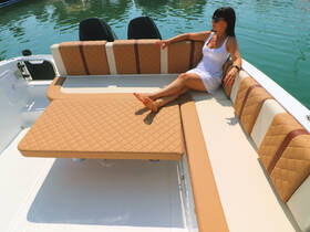 A stylish lounge area on a boat featuring comfortable seating, perfect for relaxing on the water. A woman enjoys the sun, showcasing the inviting interior design.
