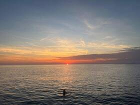 A serene sunset view over calm waters with a person swimming, capturing the essence of a perfect evening on the water.
