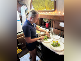 A chef prepares fresh salads in the cozy interior of a boat's galley, showcasing the charm of onboard dining experiences.