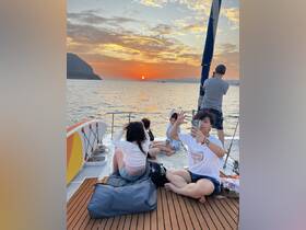 A lively group enjoys a stunning sunset aboard a yacht, capturing memories with smiles and photos — perfect for a memorable evening on the water.