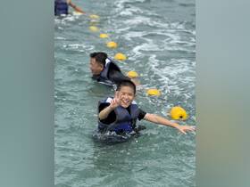 A joyful child gives a peace sign while swimming in the ocean, enjoying a fun day out with family. This captures the essence of water activities and family bonding.