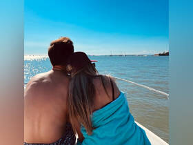 A couple enjoys a romantic moment on a boat, embracing while taking in the beautiful water views under a clear blue sky.