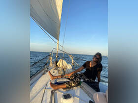 A person enjoys a relaxing moment aboard a sailboat, soaking in the sunset and the serene waters — a perfect scene for sailing enthusiasts.