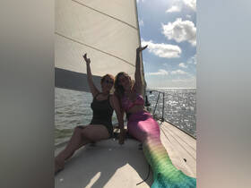 Two friends celebrate on a sailboat, showcasing a fun mermaid costume and enjoying the sun — perfect for memorable sailing adventures.