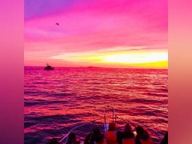 A stunning sunset view from a boat with a group of people enjoying the vibrant colors of the ocean — perfect for memorable evening cruises.