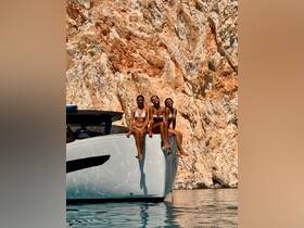 Three friends enjoy a sunny day on the bow of a sleek boat, capturing the essence of summer fun and friendship against a stunning rocky backdrop.
