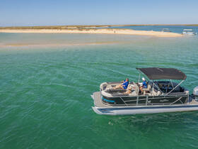 A group enjoys a relaxing day on a pontoon boat near a sandy beach, perfect for sunbathing and socializing in the beautiful turquoise waters.