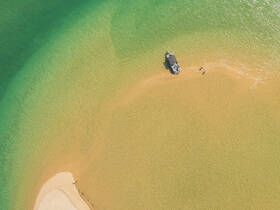 An aerial view of a boat anchored at a sandbar, with people enjoying the shallow waters — a perfect scene for a relaxing day on the beach.