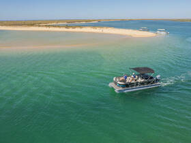 A pontoon boat glides through clear turquoise waters, with a sandy island in the background, perfect for a day of exploration and relaxation on the water.